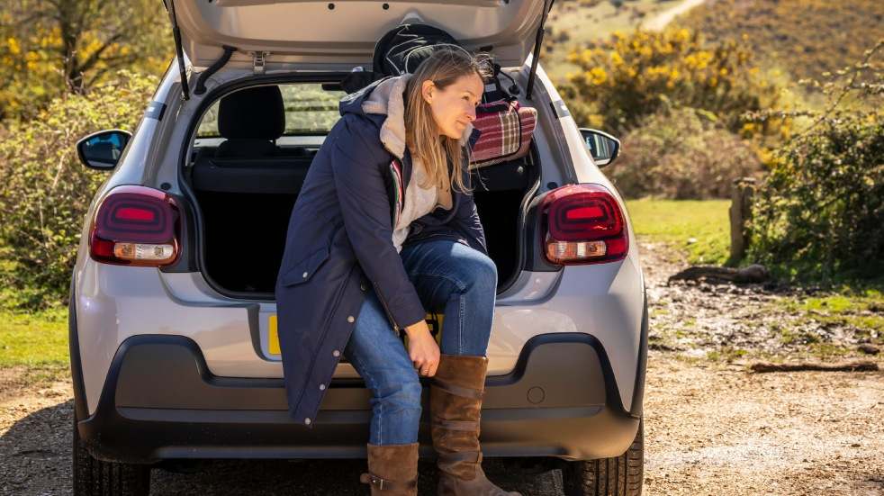 Woman sat on trunk of car putting on boots